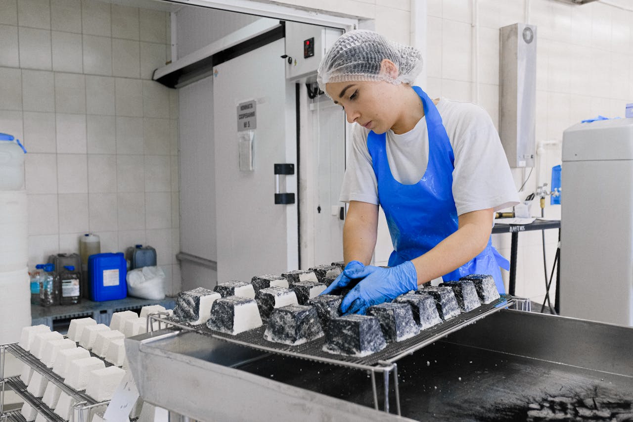 Woman in a blue apron and gloves making white cheese in a kosher-certified food factory.